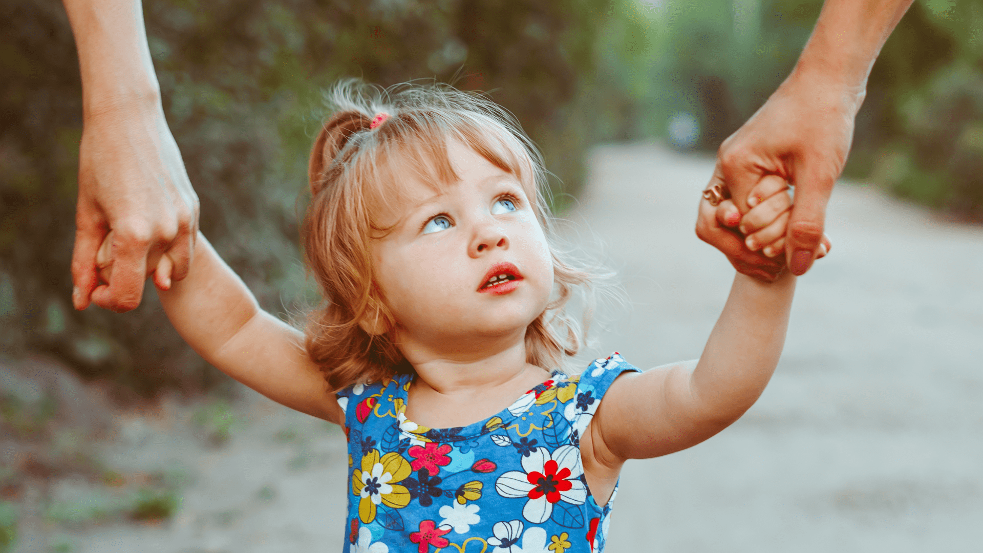 Child holding two adults' hands looking up.